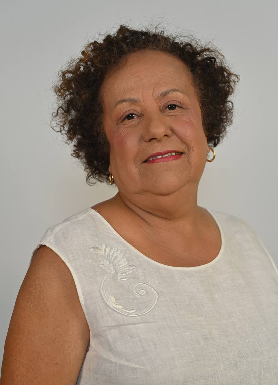 Verinha Preta, mulher negra de 71 anos, cabelo curto e cacheado, blusa branca, sorrindo.
